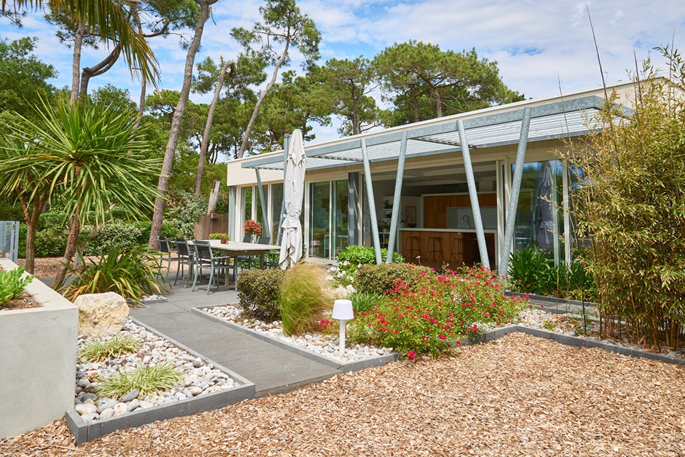 Terrasse ensoleillée, devant une maison d'architecte et une pergola métallique. Extérieur style bord de mer et sud de la France.