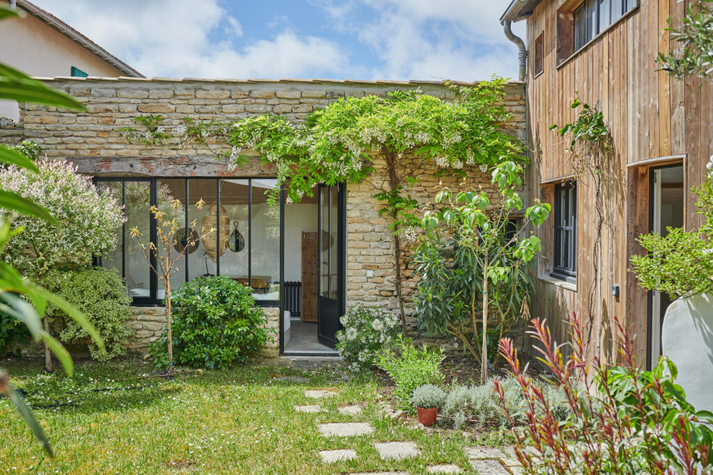 Façade de maisonnette typé en pierre. Porte fenêtre et verrière moderne. Cour végétale et luxuriante.