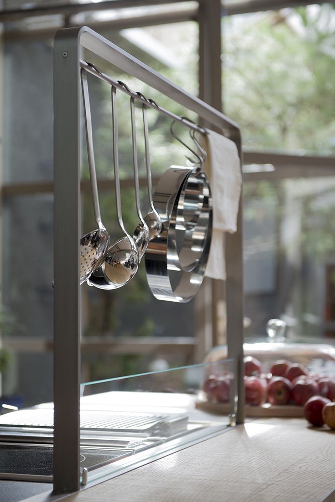 Détail dans une cuisine de la marque ARTHUR BONNET, modèle Métisse, réalisé en 3D. Au dessus d'un plan de travail sont suspendus des louches, écumoirs et autres accessoires de cuisine. Des fruits posés au 2nd plan.