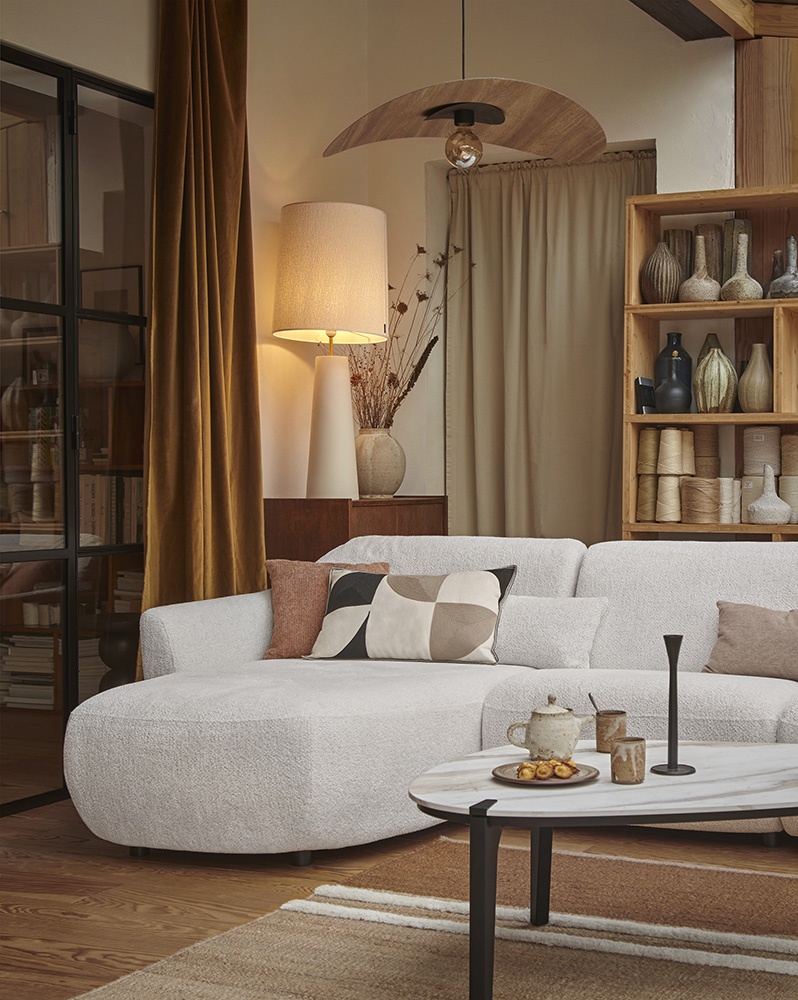 Ambiance dans un salon avec un canapé écru , une table basse beige, mobilier Gautier, ligne Oasis. A l'arrière plan : une étagère avec une accumulation de vases en céramiques. Le tout est dans une ambiance cosy monochrome.