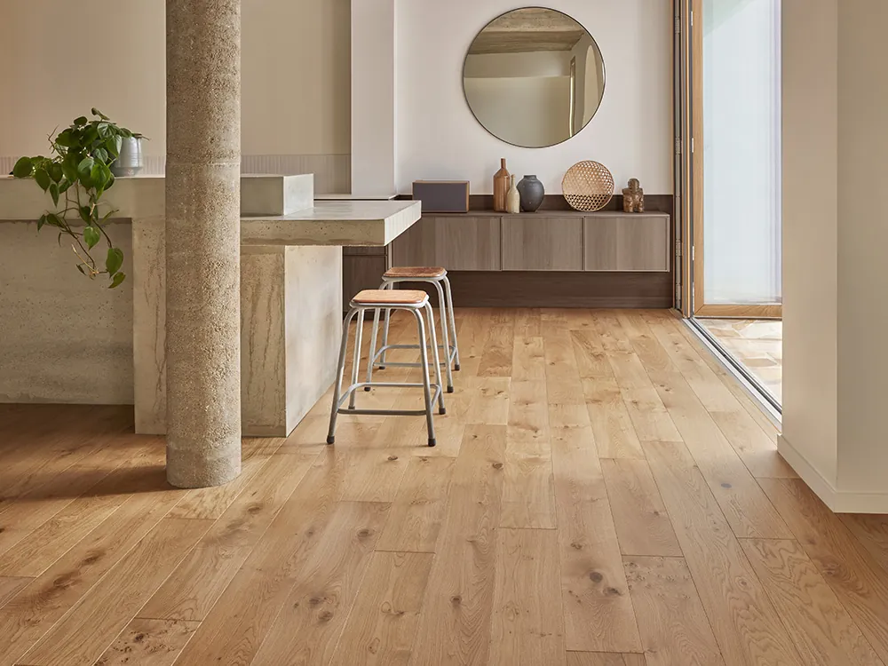 Ambiance intérieure design : un espace repas en travertin avec 2 tabourets, une enfilade suspendue sur le mur du fond avec des accessoires choisis de décoration. Ambiance chaleureuse de part le sol en parquet PANAGET et lumière douce.